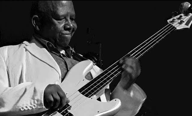 A still from a classic Spencer Mbadu performance, in complete harmony with his bass guitar. By John Wilpers.